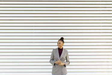 Businesswoman looking away while standing against striped wall - JSMF01994