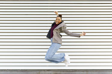 Carefree businesswoman with arms outstretched jumping against white wall - JSMF01995