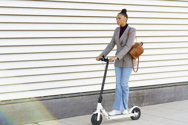 Geschäftsfrau mit Tasche, die auf einem elektrischen Roller auf dem Gehweg fährt - JSMF01999
