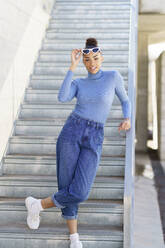 Junge Frau mit Sonnenbrille starrt, während sie gegen eine Treppe steht - JSMF02003
