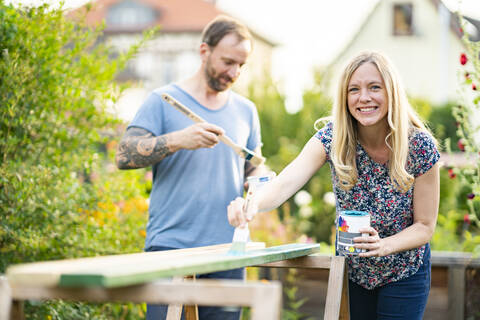 Blonde Frau, die mit ihrem Freund im Garten stehend Holzbretter bemalt, lizenzfreies Stockfoto