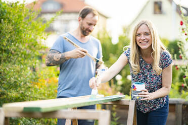 Blonde Frau, die mit ihrem Freund im Garten stehend Holzbretter bemalt - AKLF00090