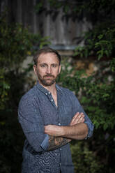 Bearded man standing with arms crossed in garden - AKLF00100