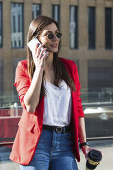 Female entrepreneur in sunglasses holding coffee cup while talking on smart phone - PNAF00886