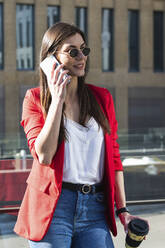 Unternehmerin mit Sonnenbrille, die eine Kaffeetasse hält, während sie mit einem Smartphone telefoniert - PNAF00886