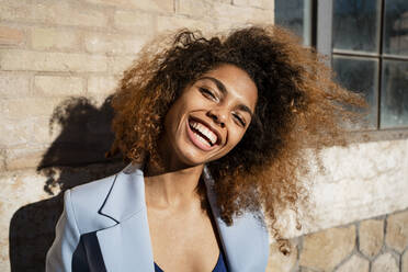 Fröhliche Afro-Frau mit braunem Haar vor einem Gebäude - RCPF00747