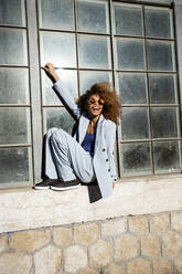 Cheerful young woman sitting while balancing on window sill - RCPF00752