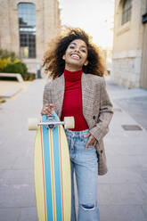 Smiling woman with skateboard standing on footpath - RCPF00767