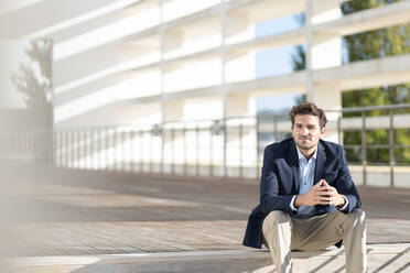 Businessman looking away while sitting on steps during sunny day - SBOF02859