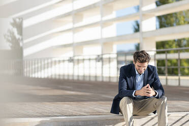 Businessman smiling while sitting on steps during sunny day - SBOF02860