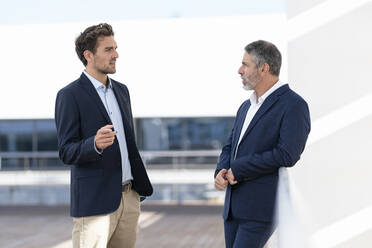 Male business people having discussion while standing at office terrace - SBOF02867