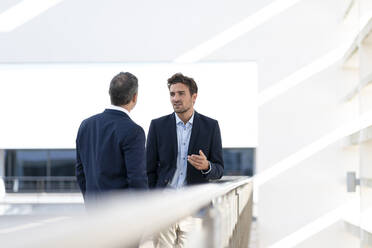 Male professionals having discussion while standing at office building terrace - SBOF02876