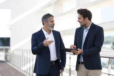 Business people discussing over digital tablet while standing at office building terrace - SBOF02879