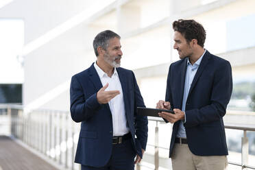 Geschäftsleute, die auf der Terrasse eines Bürogebäudes über ein digitales Tablet diskutieren - SBOF02879