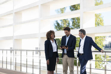 Ein professionelles Team diskutiert über ein digitales Tablet, während es an einem Geländer steht - SBOF02881