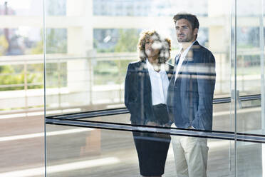 Business people looking away while standing by glass window in modern office - SBOF02888