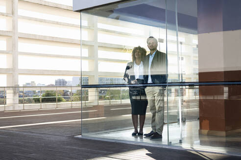 Unternehmer schauen durch ein Fenster, während sie in einem modernen Büro stehen - SBOF02889