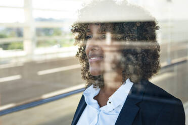 Weibliche Unternehmerin schaut durch ein Fenster, während sie in einem modernen Büro steht - SBOF02892