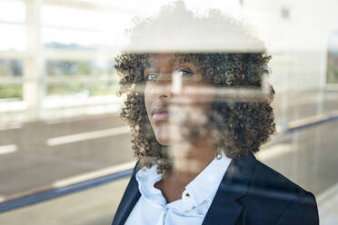 Contemplating businesswoman looking through window while standing in modern office - SBOF02893