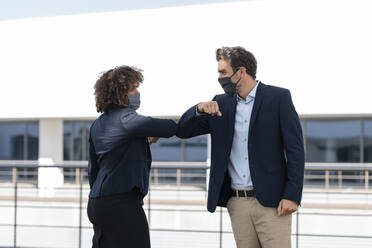 Colleagues giving elbow bump while greeting at office building terrace - SBOF02898