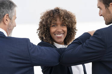 Lächelnde Geschäftsfrau stößt ihren Kollegen mit dem Ellbogen an, während sie an einer weißen Wand steht - SBOF02916