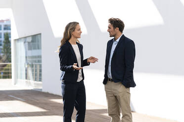 Female entrepreneur having discussion with colleague while standing against wall - SBOF02925