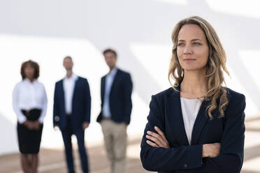 Weibliche Unternehmerin schaut weg, während sie mit Kollegen im Hintergrund auf einer Büroterrasse steht - SBOF02944