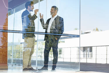 Männliche Geschäftsleute diskutieren über eine Grafik, während sie in einem modernen Büro stehen - SBOF02955