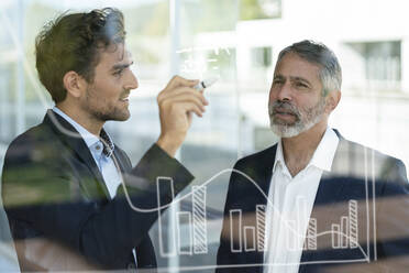 Male entrepreneur working with colleague on graph on glass at modern office - SBOF02956