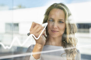 Female entrepreneur drawing on glass window while working at modern office - SBOF02959