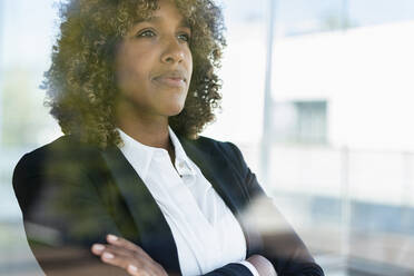 Confident businesswoman looking away while standing with arms crossed at office - SBOF02971
