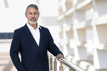 Mature businessman staring while standing by railing at office terrace - SBOF02981