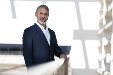 Smiling entrepreneur standing by railing at office terrace - SBOF02982