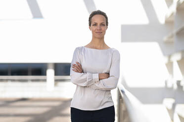 Confident businesswoman with arms crossed standing at office building terrace - SBOF03004