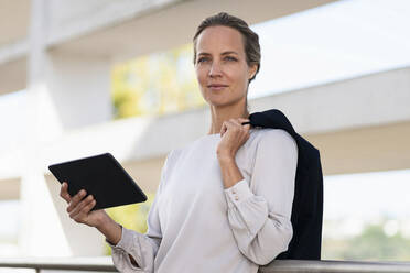 Female entrepreneur with digital tablet and jacket standing at office terrace - SBOF03009