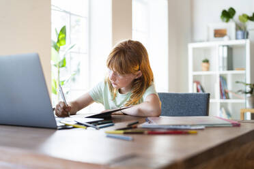 Concentrated redhead girl doing homework in front of laptop at home - SBOF03024