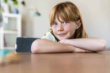 Smiling redhead girl with blue eyes sitting at table in living room - SBOF03033