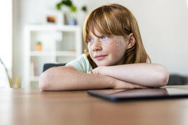 Thoughtful redhead girl looking away while sitting at table in living room - SBOF03035