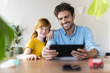 Father with redhead daughter smiling and looking at digital tablet together in living room - SBOF03036