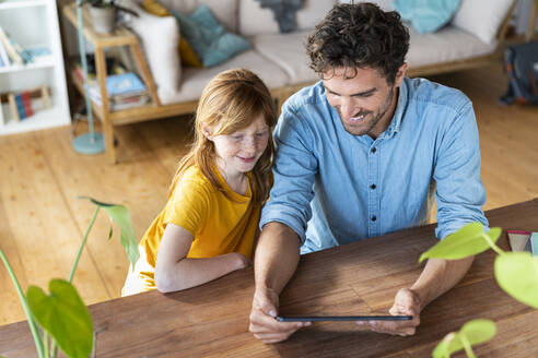 Lächelnder Vater und Tochter schauen auf ein digitales Tablet, während sie im Wohnzimmer sitzen - SBOF03039