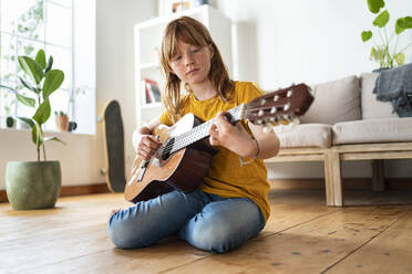 Nettes rothaariges Mädchen spielt Gitarre im Wohnzimmer zu Hause - SBOF03046