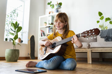 Rothaariges Mädchen lernt online über ein digitales Tablet Gitarre, während sie zu Hause auf dem Boden sitzt - SBOF03048