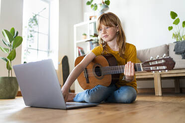 Redhead girl using laptop while learning guitar at home - SBOF03051