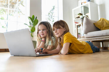 Freundinnen benutzen einen Laptop, während sie zu Hause auf dem Boden liegen - SBOF03054