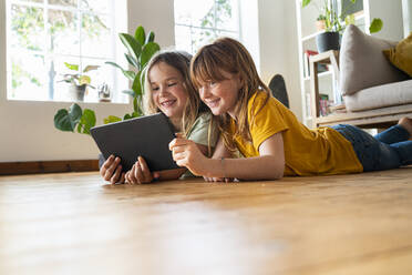 Smiling girls looking at digital tablet together while lying on front at home - SBOF03058