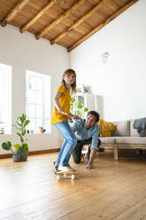 Father assisting daughter to ride skateboard at home - SBOF03064