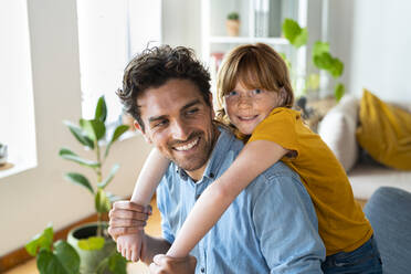 Smiling daughter cuddling father at home - SBOF03065