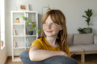 Smiling redhead girl looking away while sitting on chair at home - SBOF03072