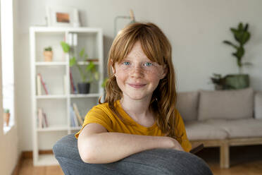 Smiling redhead girl with blue eyes sitting on chair at home - SBOF03073