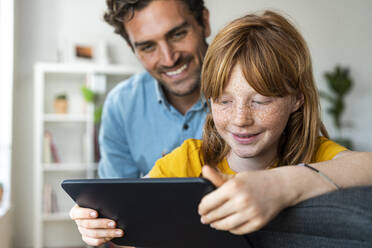 Father and cute redhead daughter looking at tablet together in living room at home - SBOF03079